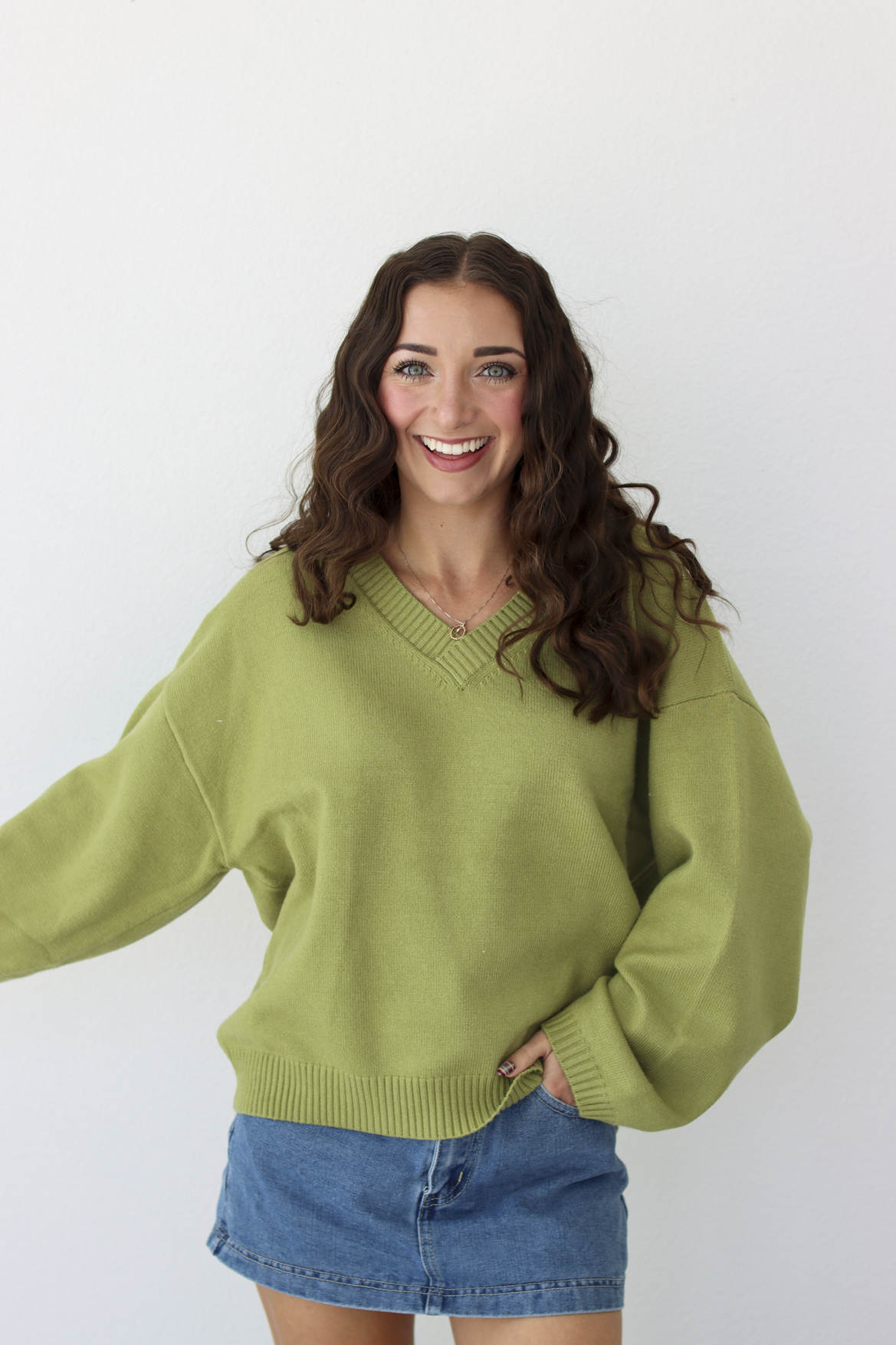 Woman wearing a v-neck green sweater with a blue denim mini skirt 