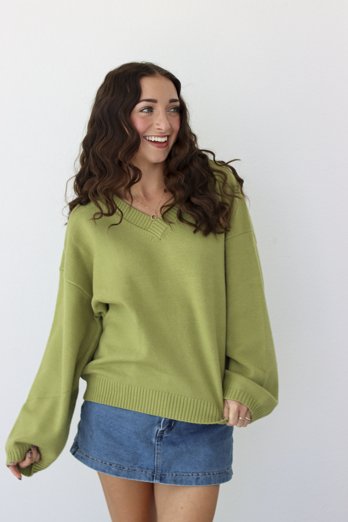 Woman wearing a v-neck green sweater with a blue denim mini skirt 