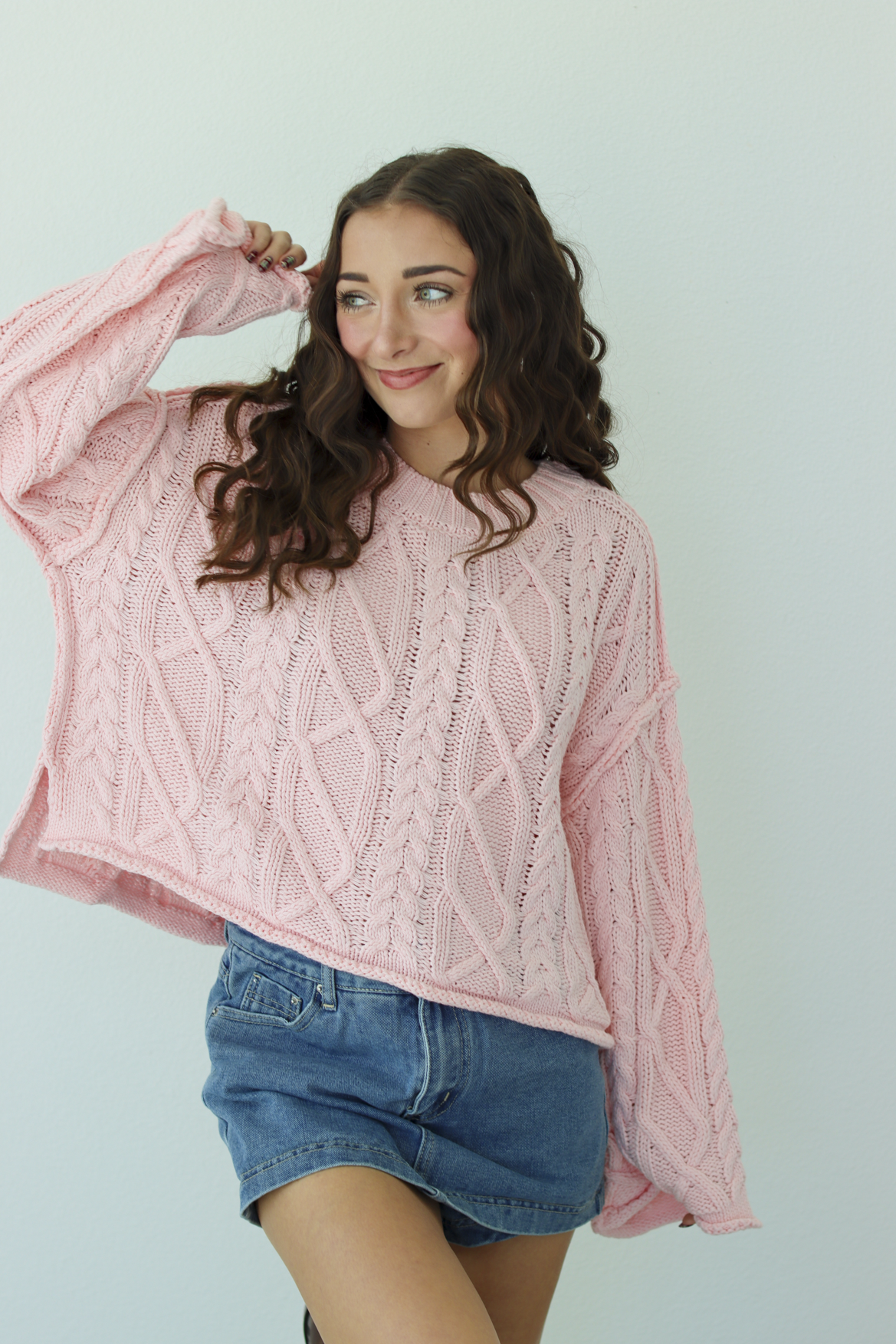 Woman wearing a pink knit sweater with a blue denim mini skirt 
