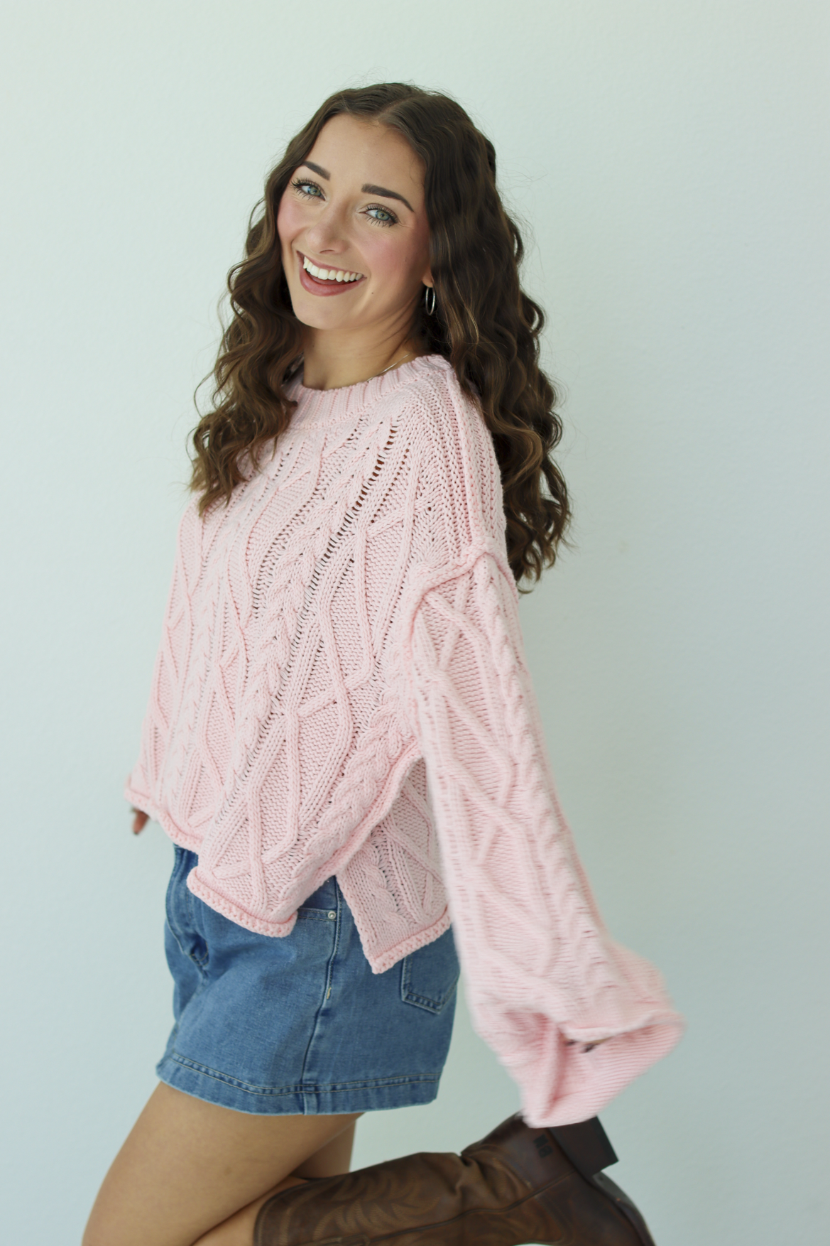Woman wearing a pink knit sweater with a blue denim mini skirt and brown boots 