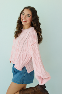 Woman wearing a pink knit sweater with a blue denim mini skirt and brown boots 