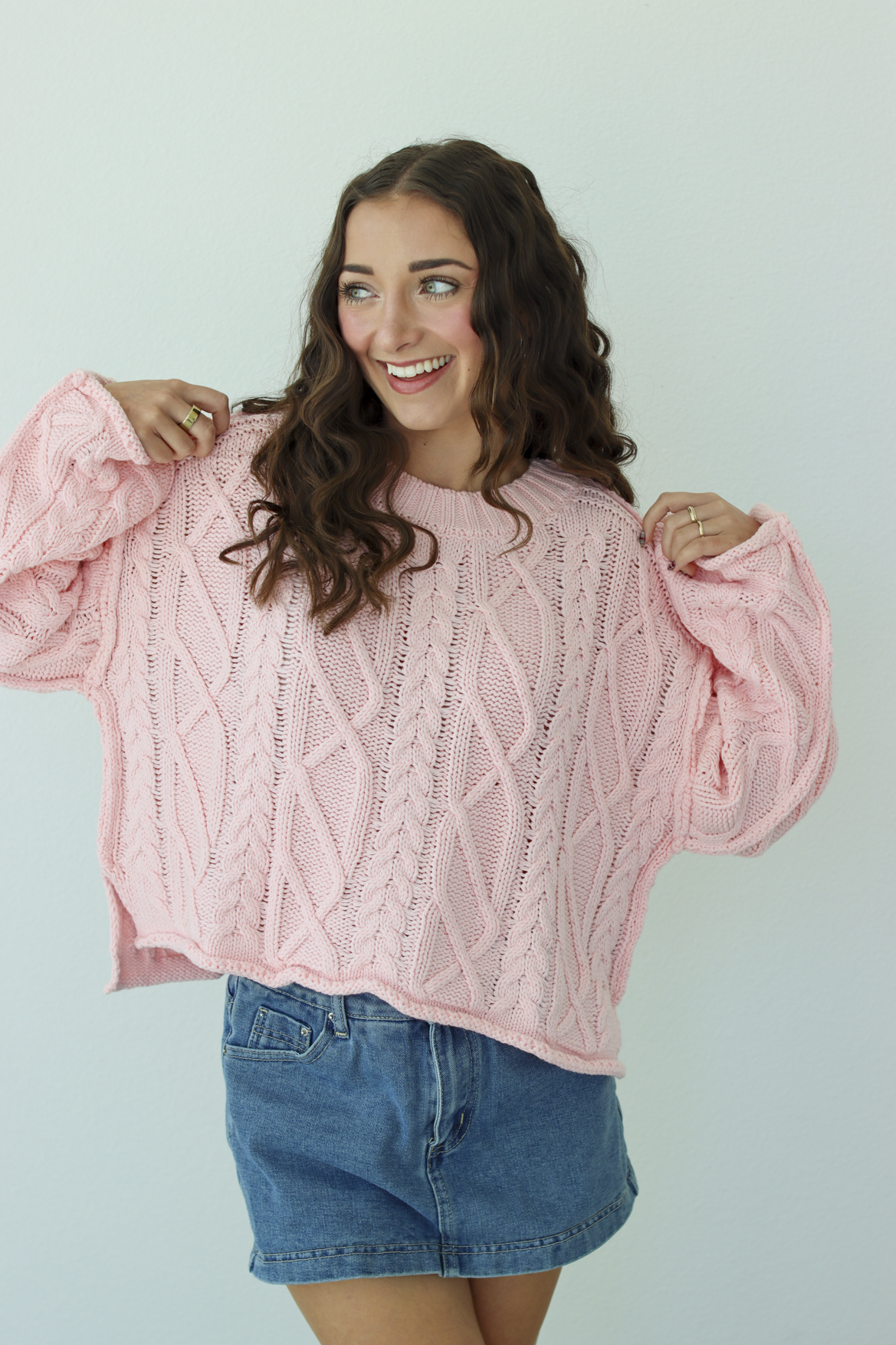 Woman wearing a pink knit sweater with a blue denim mini skirt 