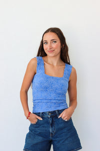 Woman wearing a blue sleeveless top and jeans against a white background