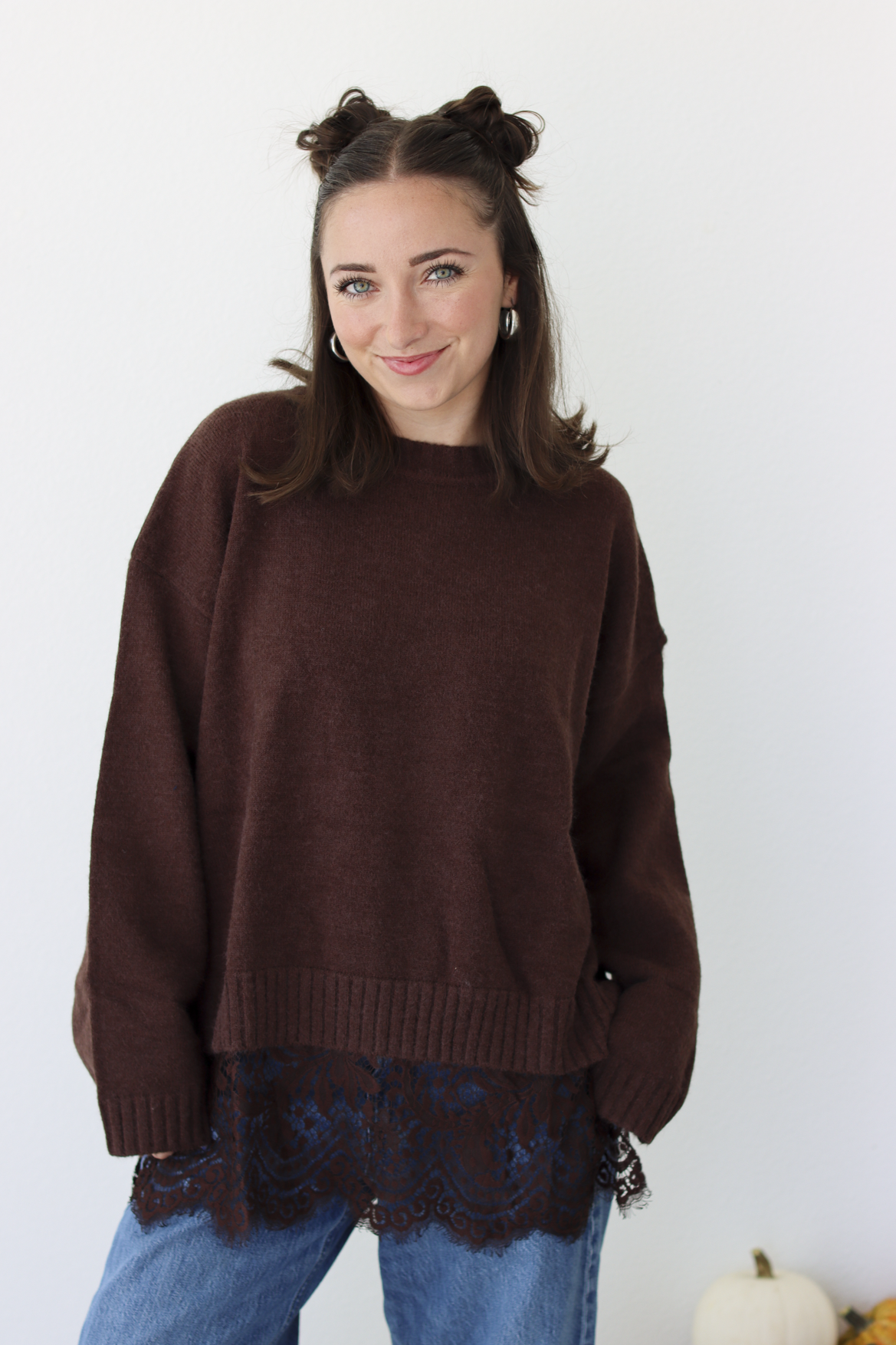 Woman wearing a brown sweater with lace trim detail at the bottom with blue denim jeans 