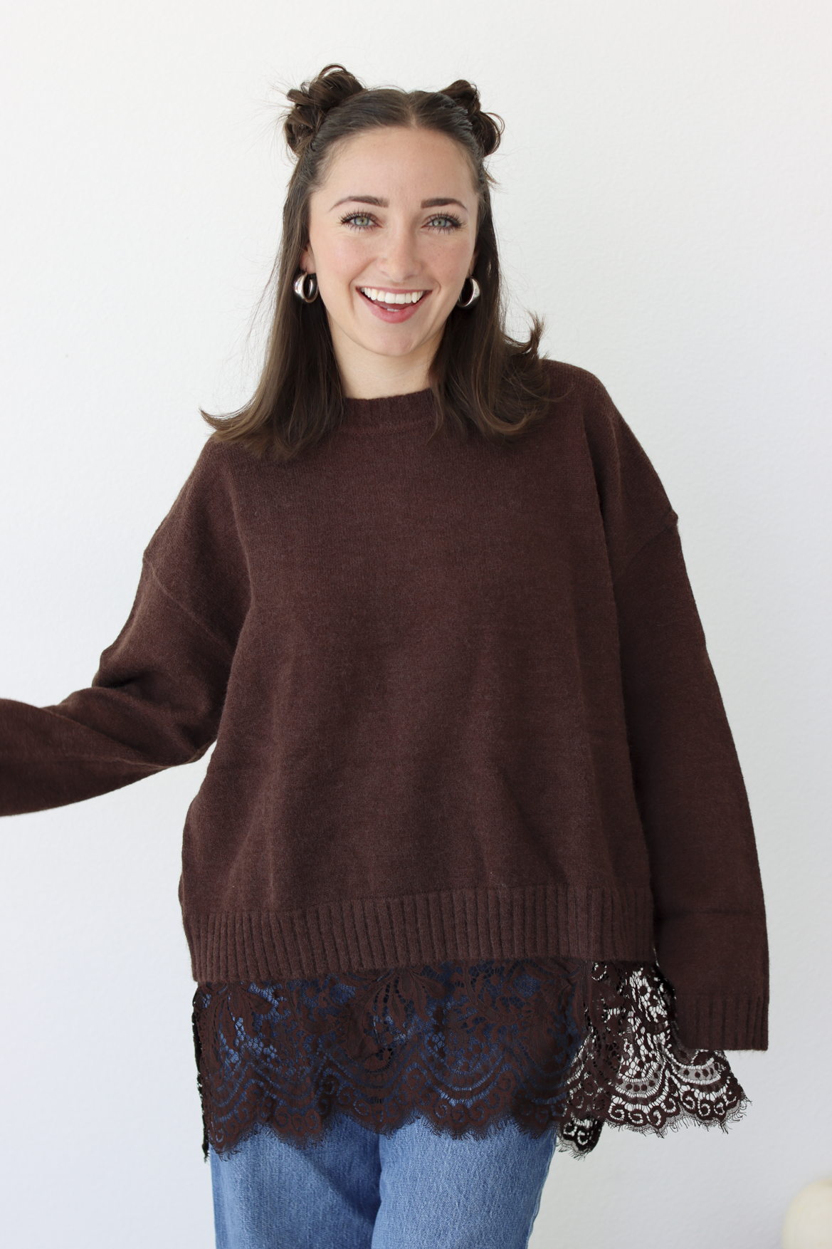Woman wearing a brown sweater with lace trim detail at the bottom with blue denim jeans 