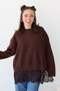 Woman wearing a brown sweater with lace trim detail at the bottom with blue denim jeans 