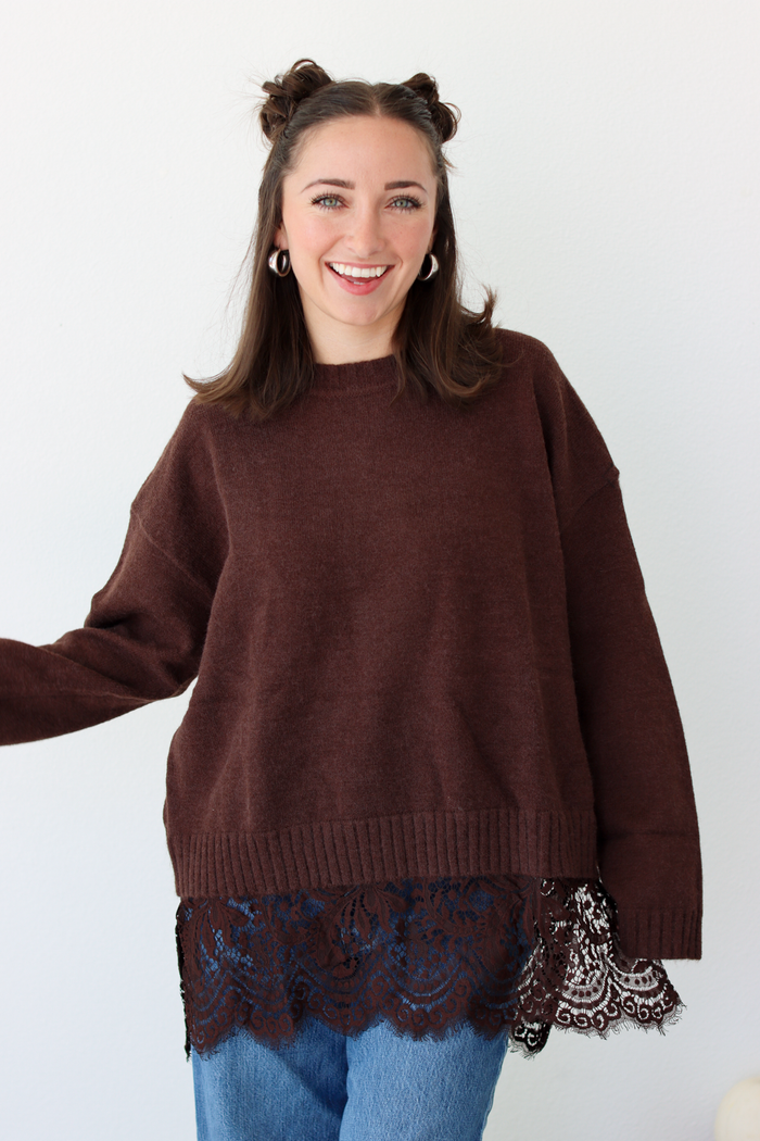 Woman wearing a brown sweater with lace trim detail at the bottom with blue denim jeans 