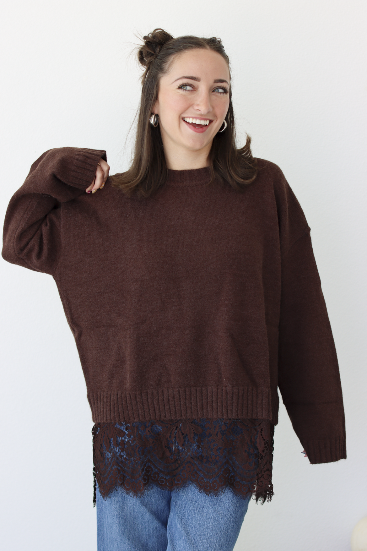 Woman wearing a brown sweater with lace trim detail at the bottom with blue denim jeans 