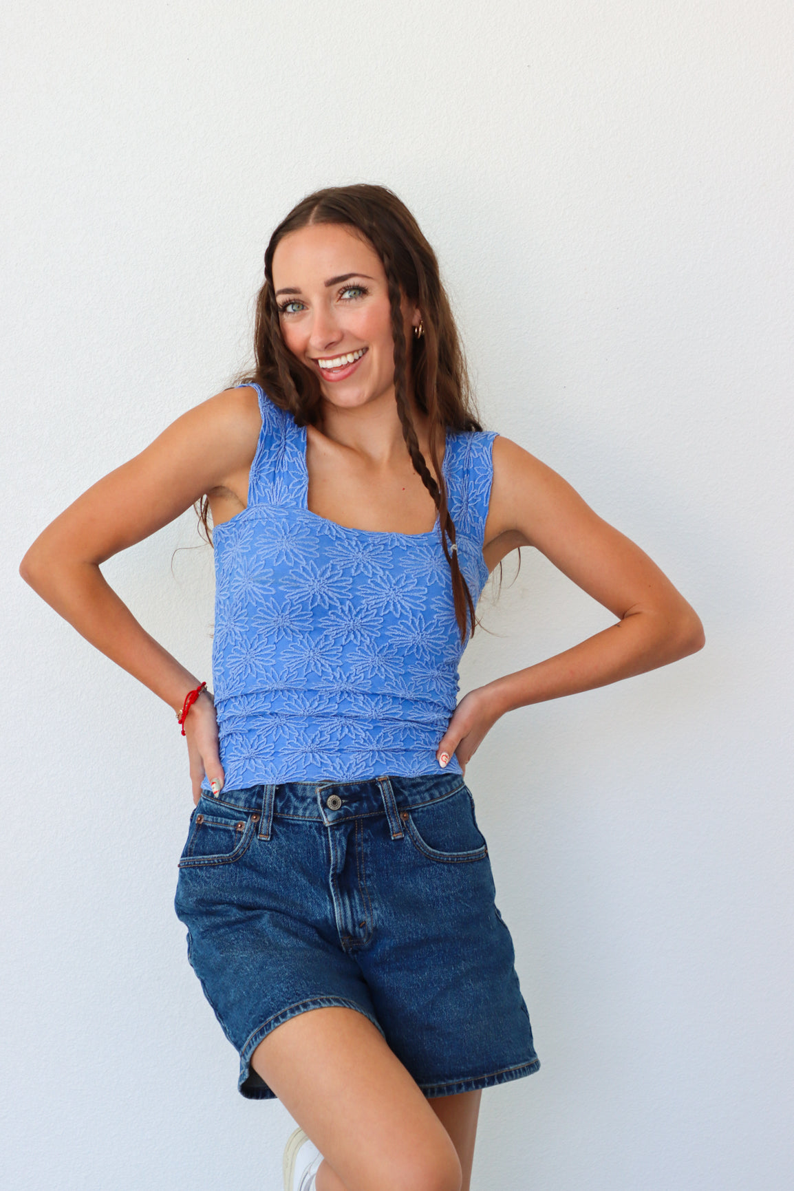 Woman wearing a blue sleeveless top and denim shorts against a white background