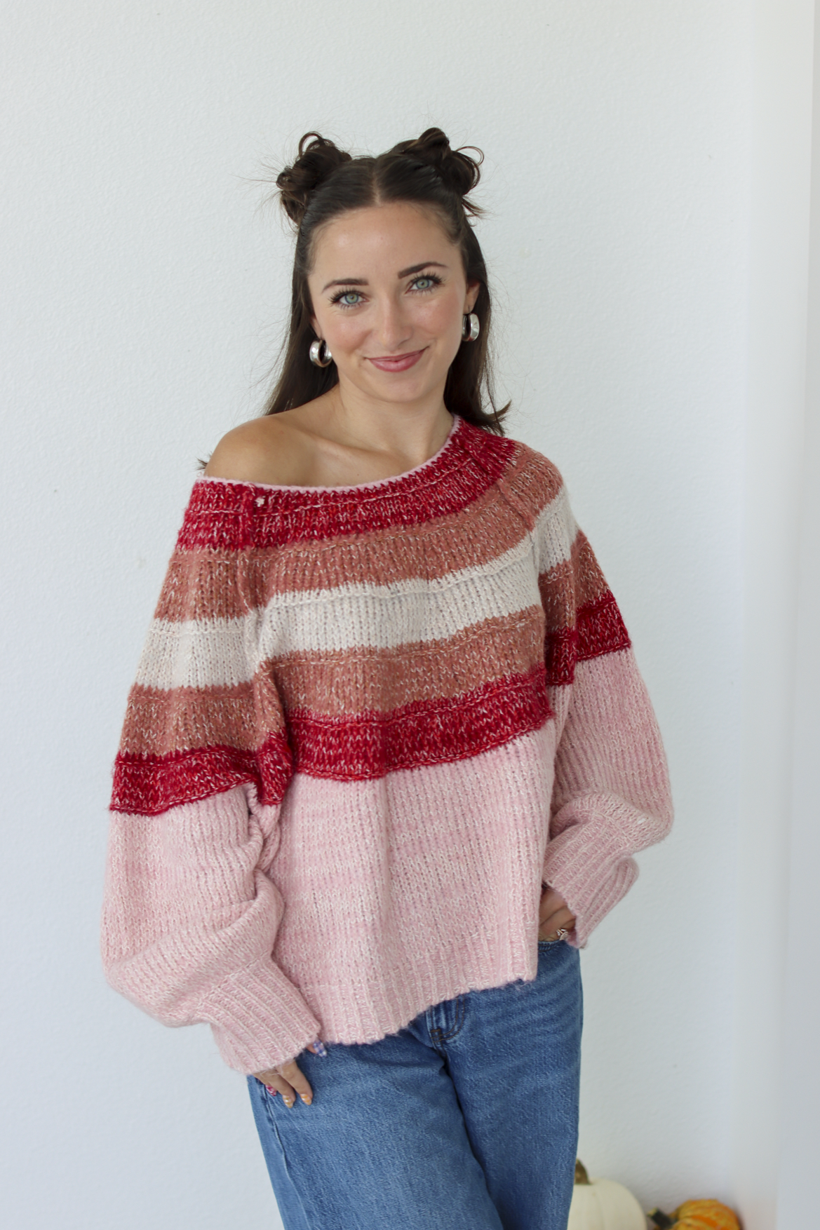 Woman wearing a pink stripe sweater off the shoulder with blue denim jeans 