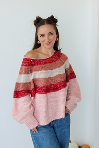 Woman wearing a pink stripe sweater off the shoulder with blue denim jeans 