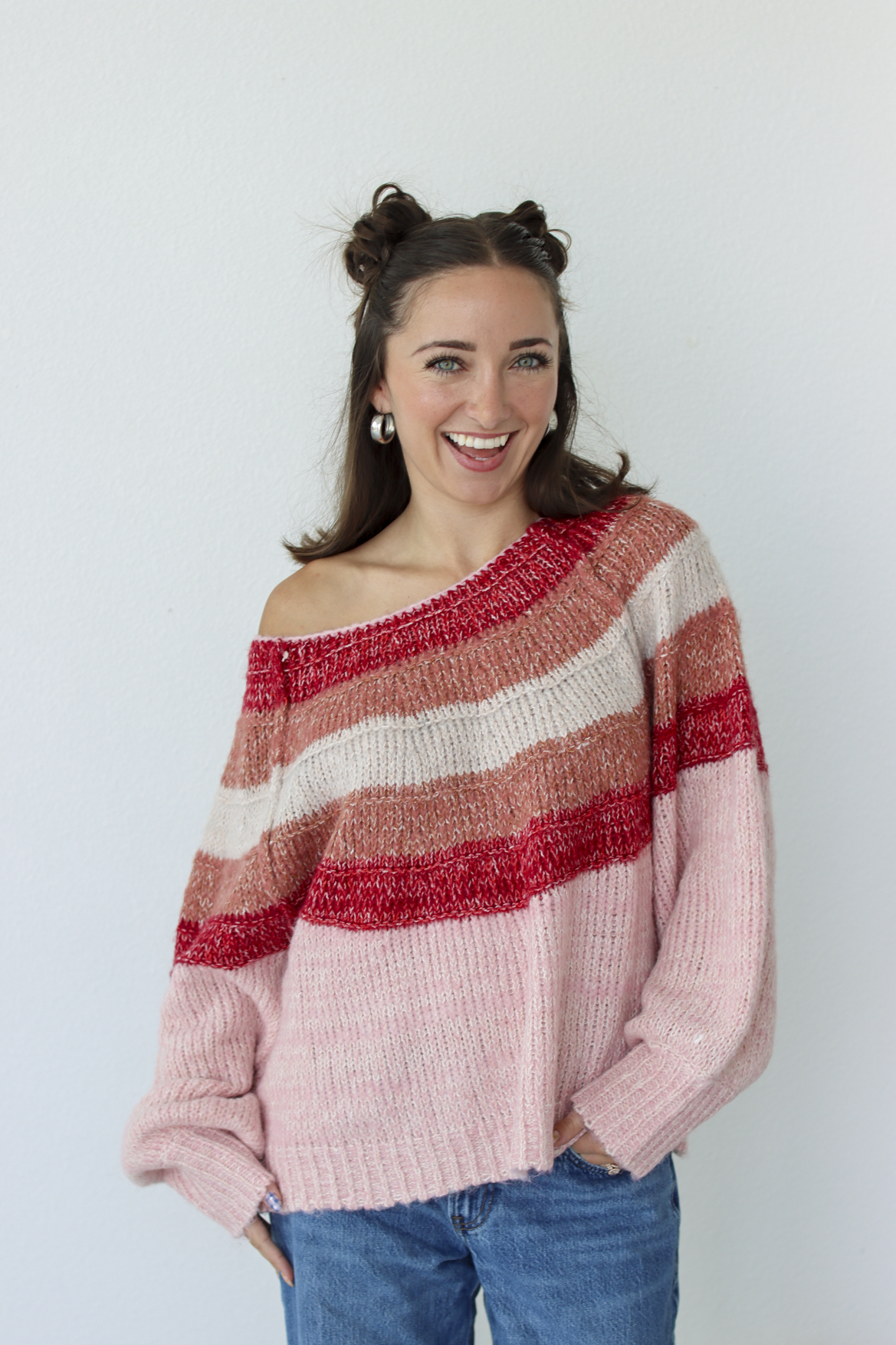 Woman wearing a pink stripe sweater off the shoulder with blue denim jeans 