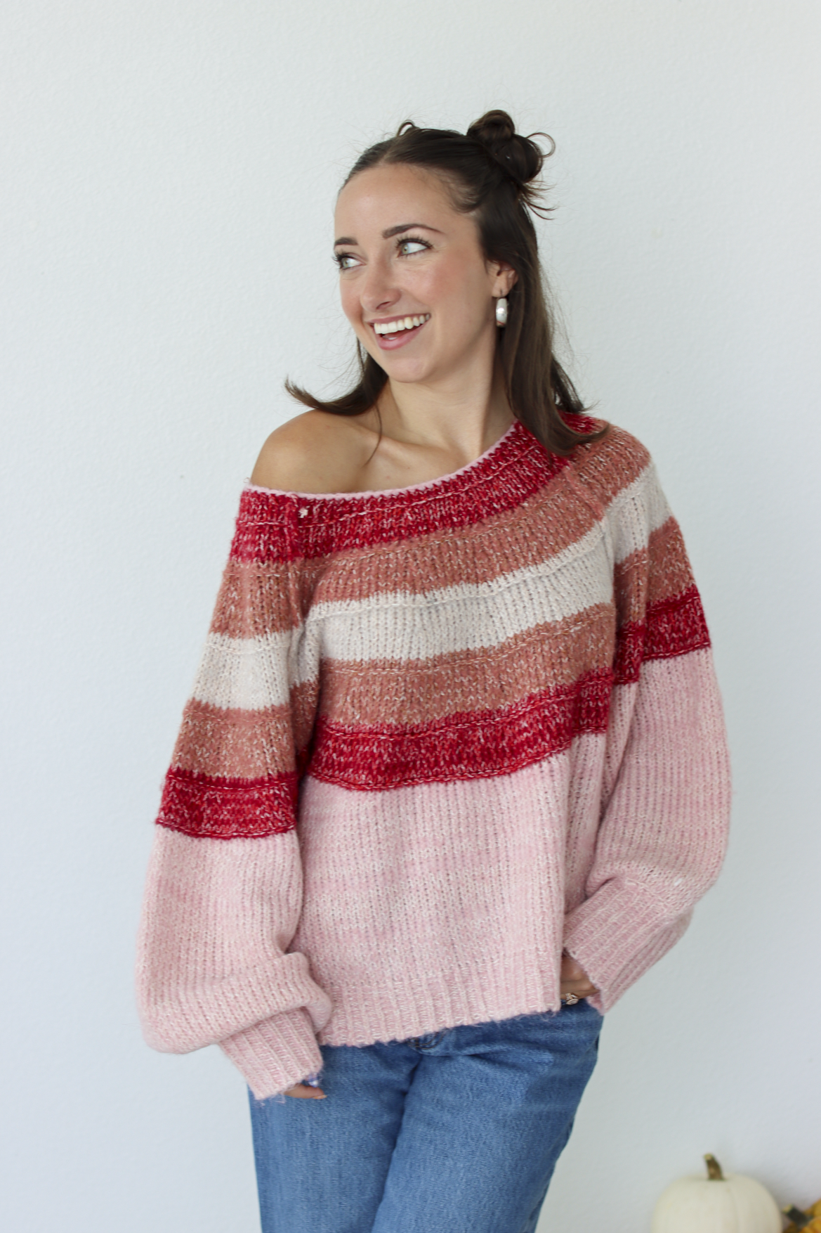 Woman wearing a pink stripe sweater off the shoulder with blue denim jeans 