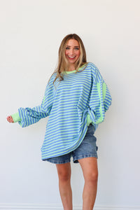 Woman wearing a blue and green striped sweater with denim shorts on a white background