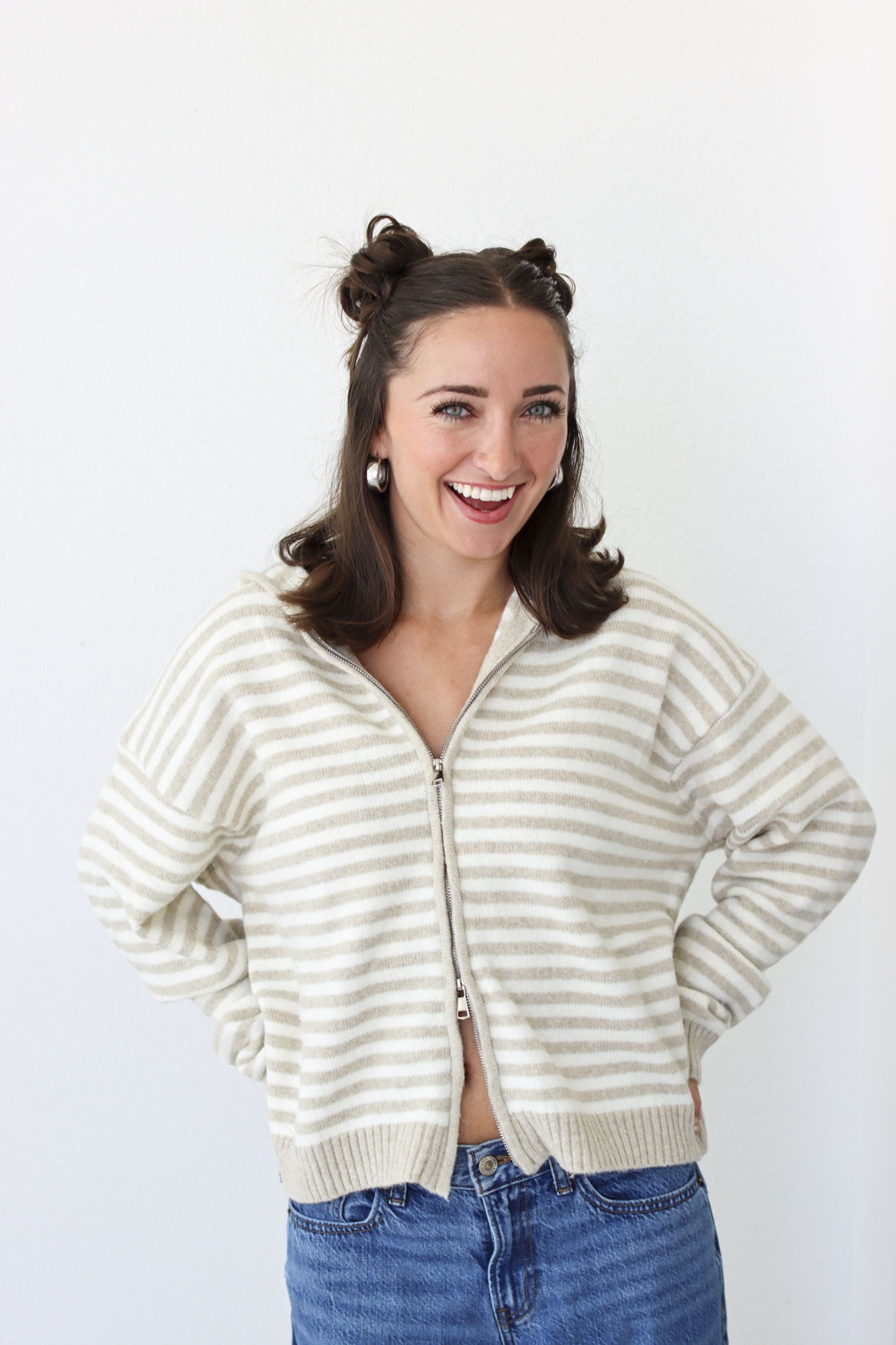 Woman wearing a tan and white striped zip-up sweater with blue denim jeans 
