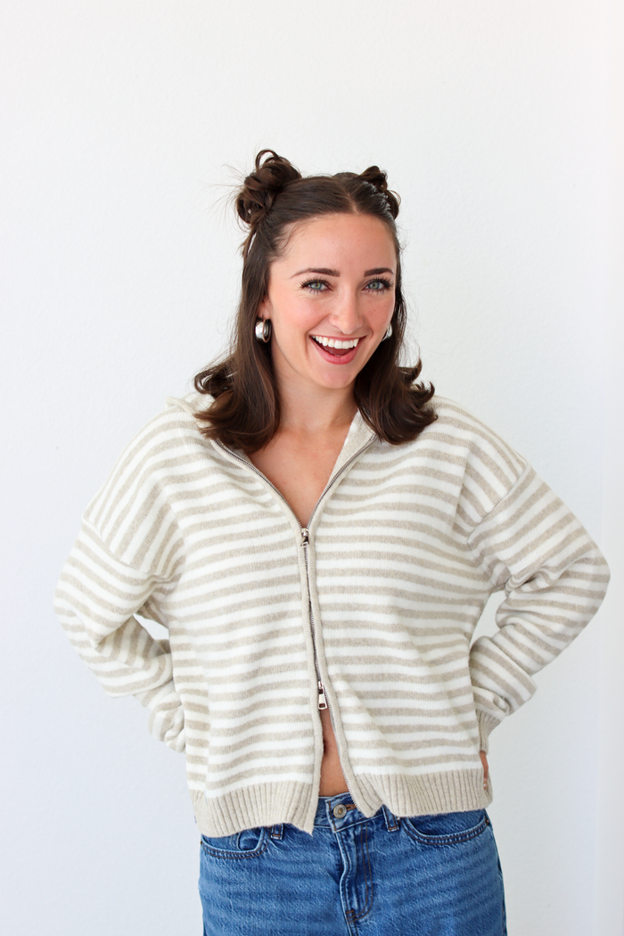 Woman wearing a tan and white striped zip-up sweater with blue denim jeans 