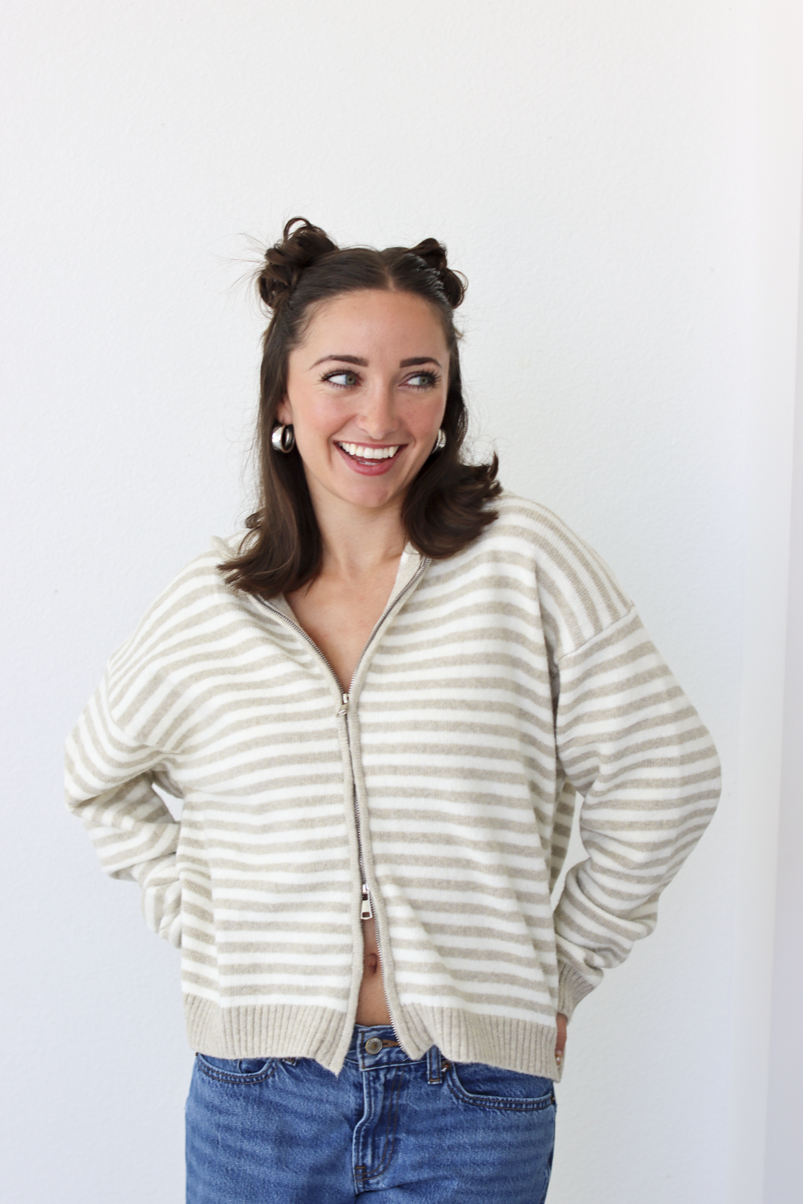 Woman wearing a tan and white striped zip-up sweater with blue denim jeans 