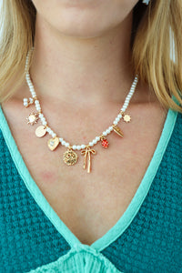 Necklace with various charms worn by a person against a teal top