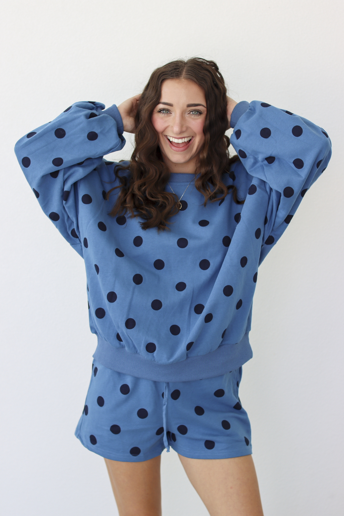 Woman wearing a blue sweater and shorts outfit set with black polka dots