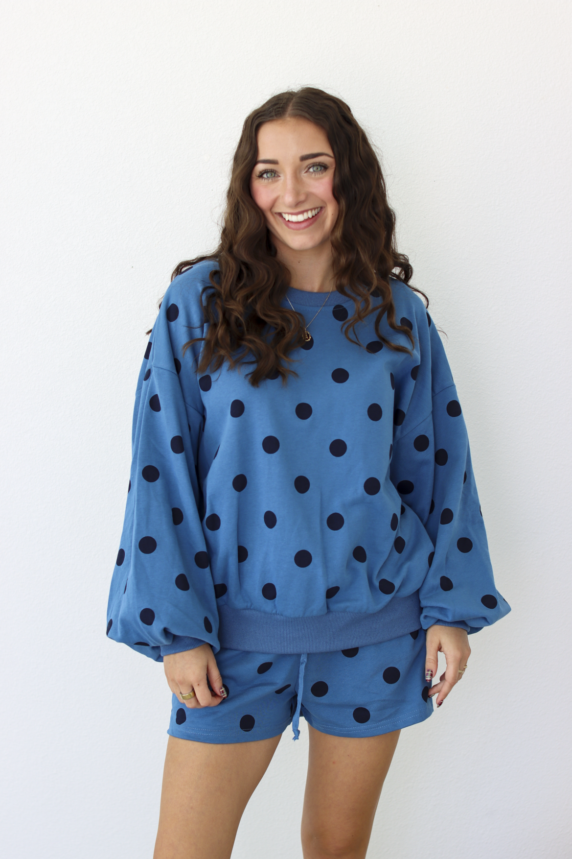Woman wearing a blue sweater and shorts outfit set with black polka dots