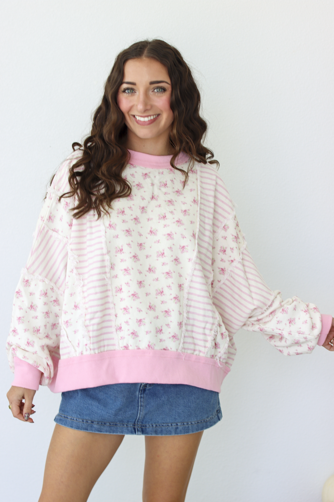 Woman wearing a pink patchwork distressed sweater with a blue denim mini skirt 