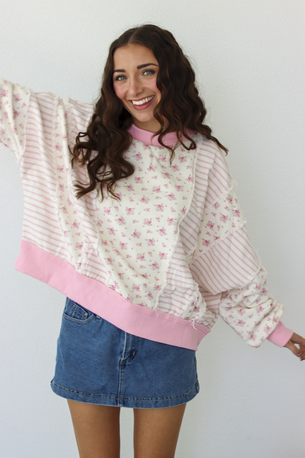 Woman wearing a pink patchwork distressed sweater with a blue denim mini skirt 