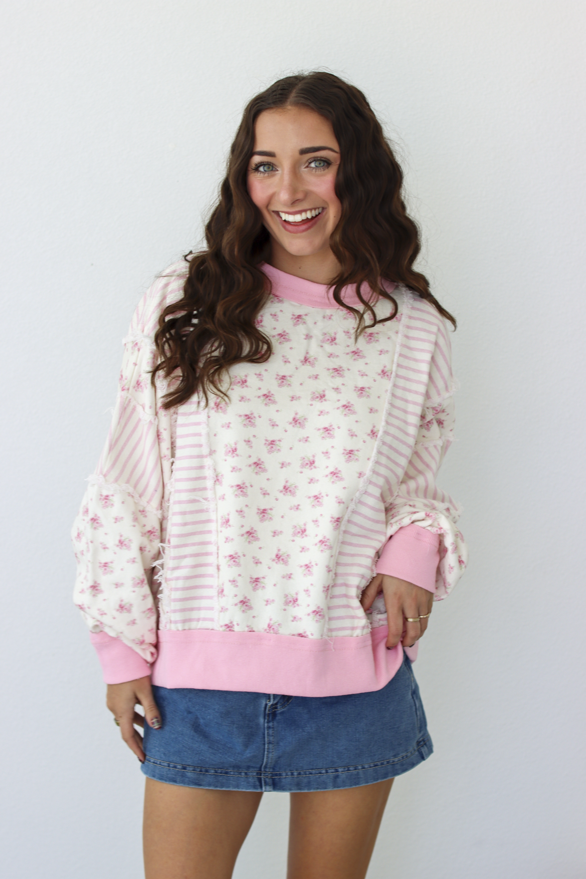 Woman wearing a pink patchwork distressed sweater with a blue denim mini skirt 