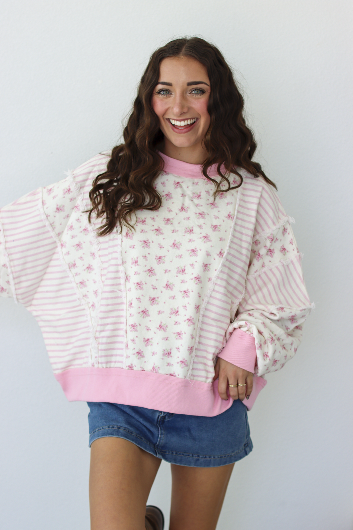 Woman wearing a pink patchwork distressed sweater with a blue denim mini skirt 