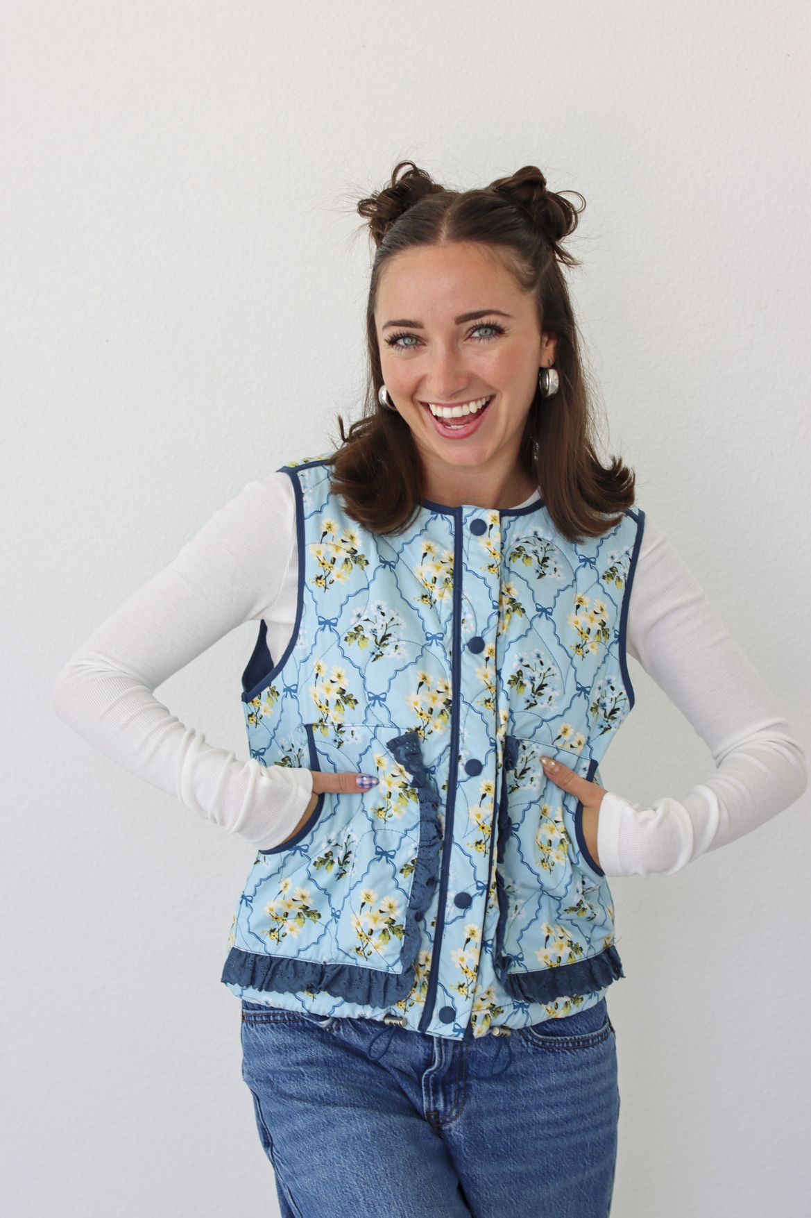 Woman wearing a blue floral puffer vest with a white long sleeve shirt and blue denim jeans 