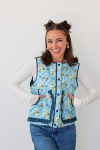 Woman wearing a blue floral puffer vest with a white long sleeve shirt and blue denim jeans 