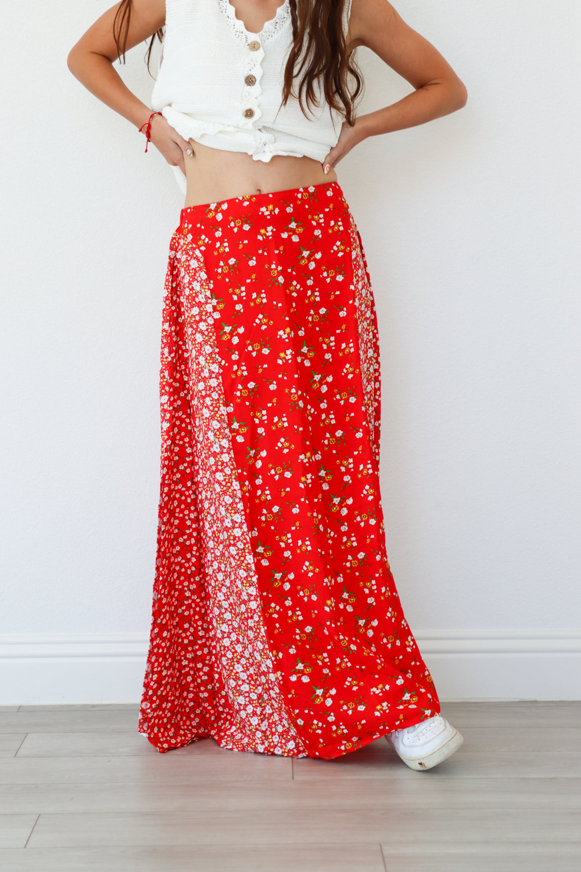 Person wearing a white top and red floral skirt on a light wooden floor.