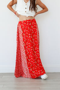 Person wearing a white top and red floral skirt on a light wooden floor.