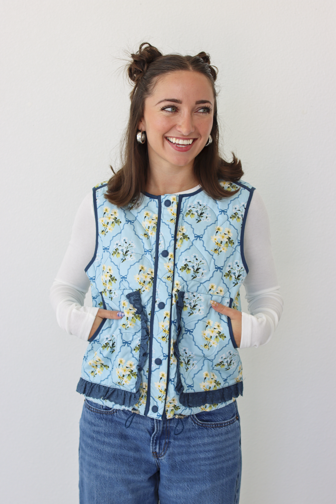Woman wearing a blue floral puffer vest with a white long sleeve shirt and blue denim jeans 