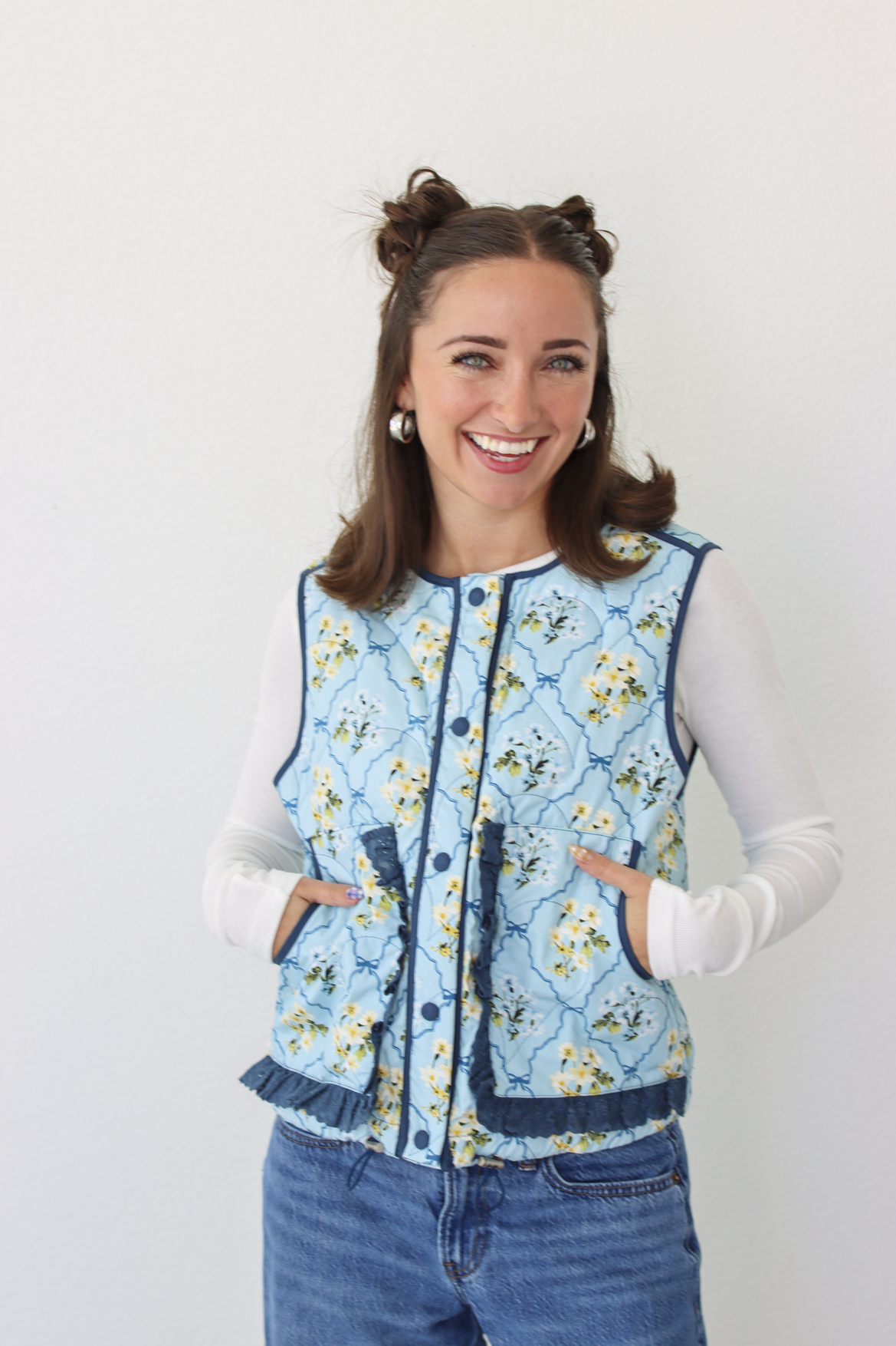 Woman wearing a blue floral puffer vest with a white long sleeve shirt and blue denim jeans 