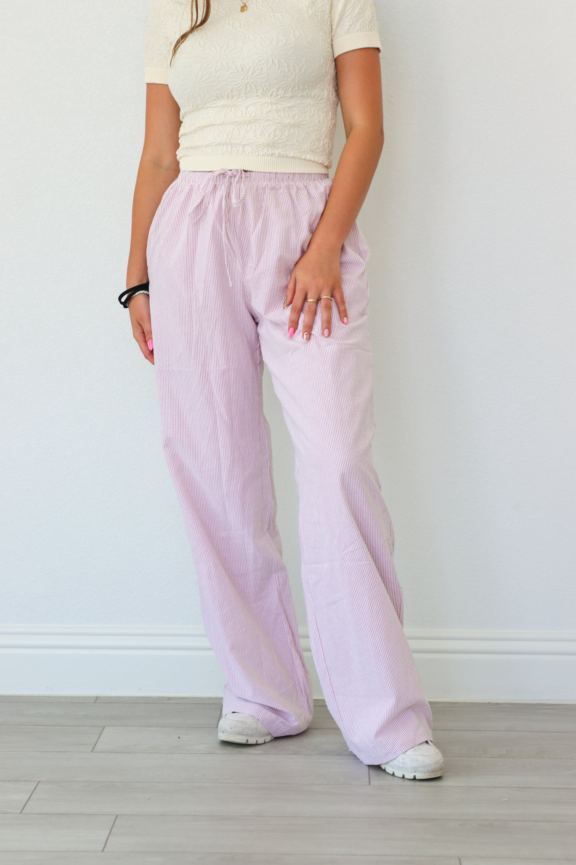 Person wearing light pink pants and a white top against a plain background
