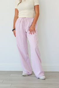 Person wearing light pink pants and a white top against a plain background