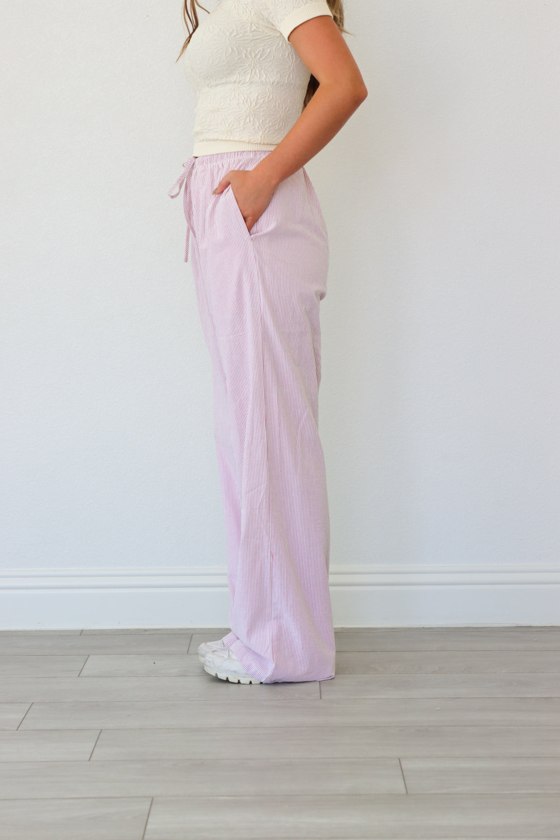 Person wearing light pink pants and a white top against a plain background