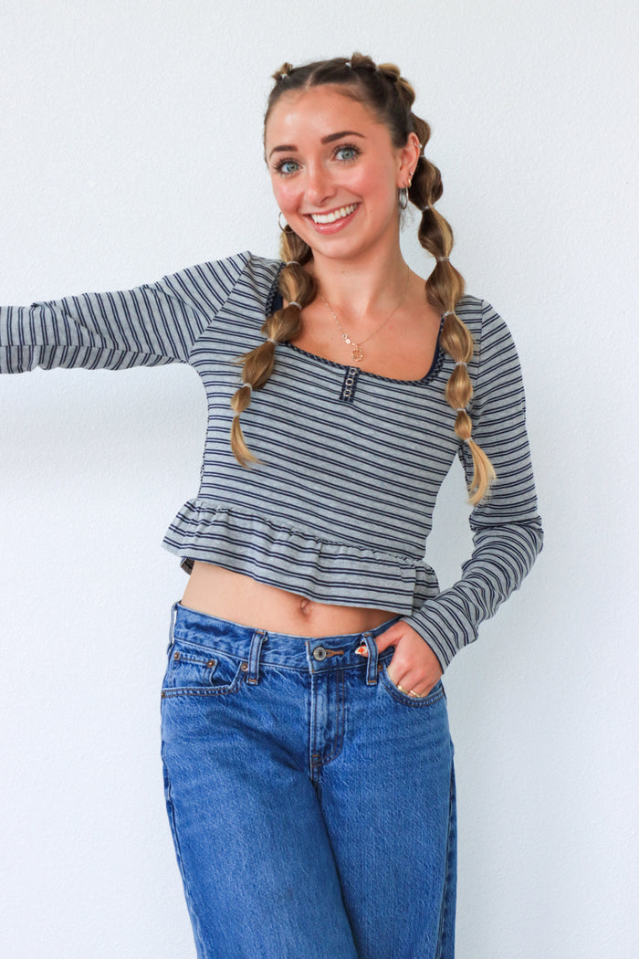 Woman wearing a striped long-sleeve top and blue jeans against a white background