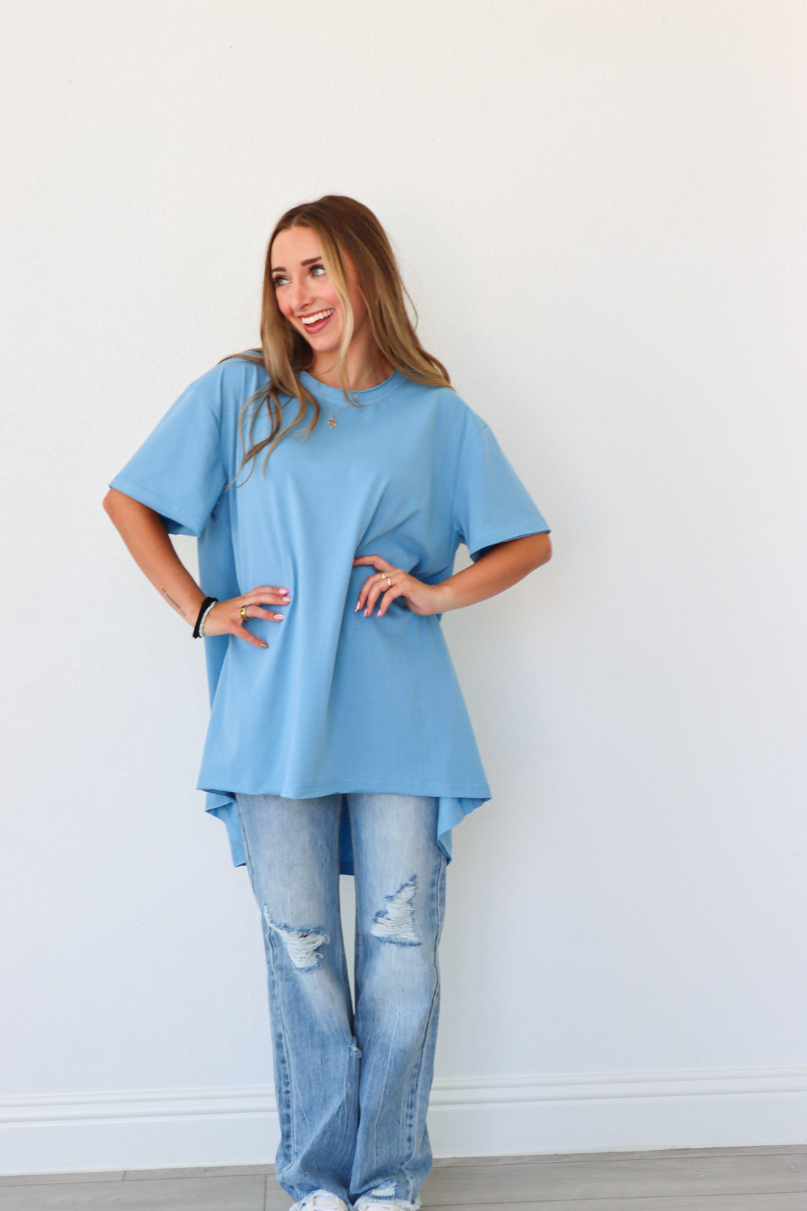 Woman wearing a light blue tunic and jeans against a white background