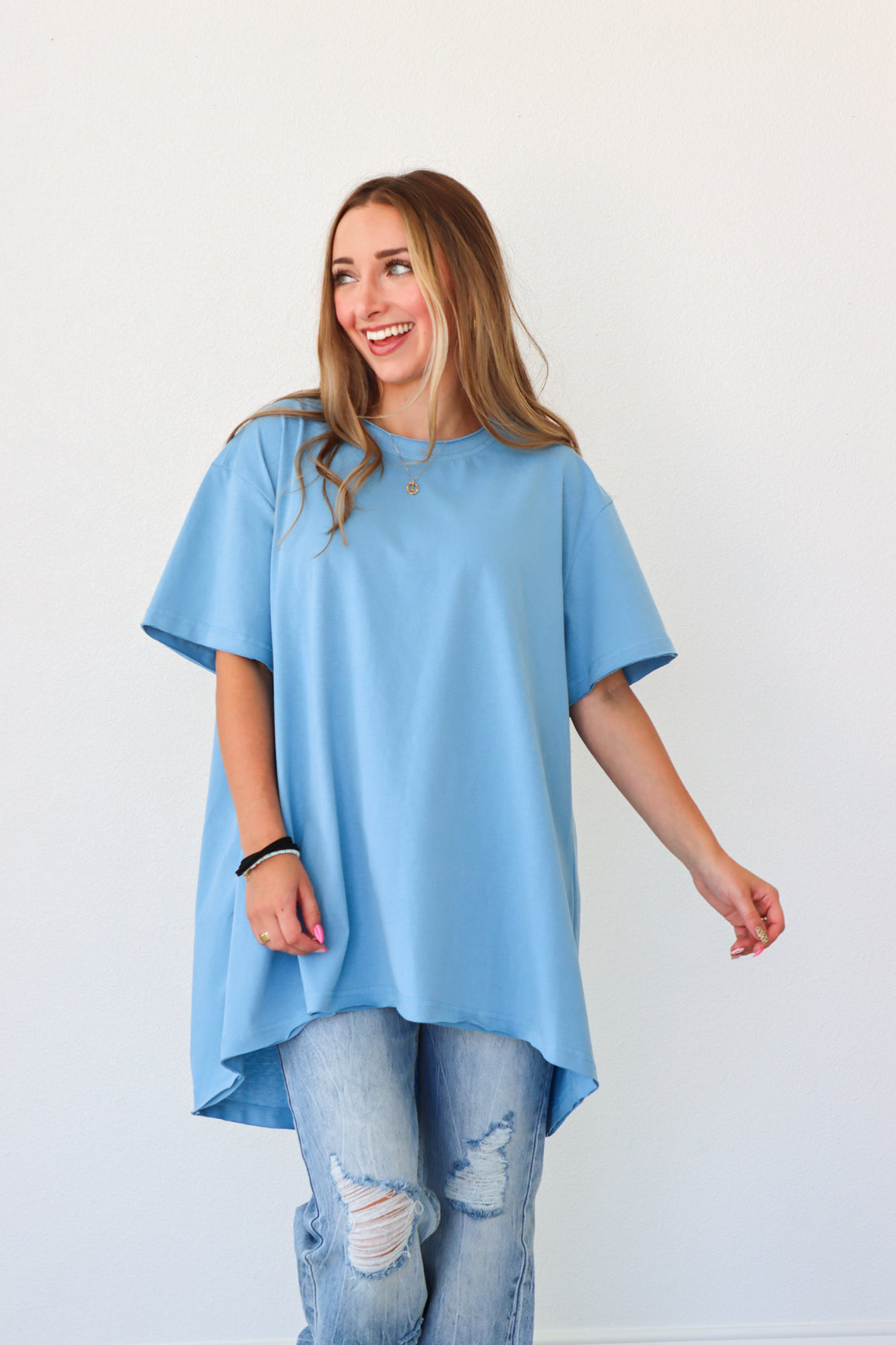 Woman wearing a blue oversized t-shirt and ripped jeans against a white background