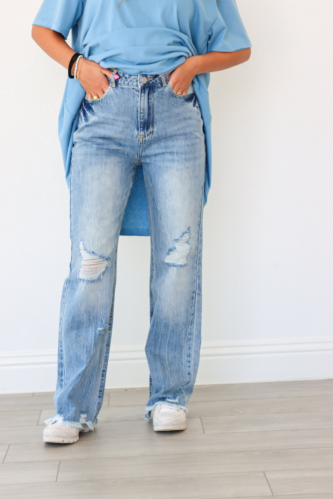 Person wearing light blue jeans and a blue shirt against a white wall.