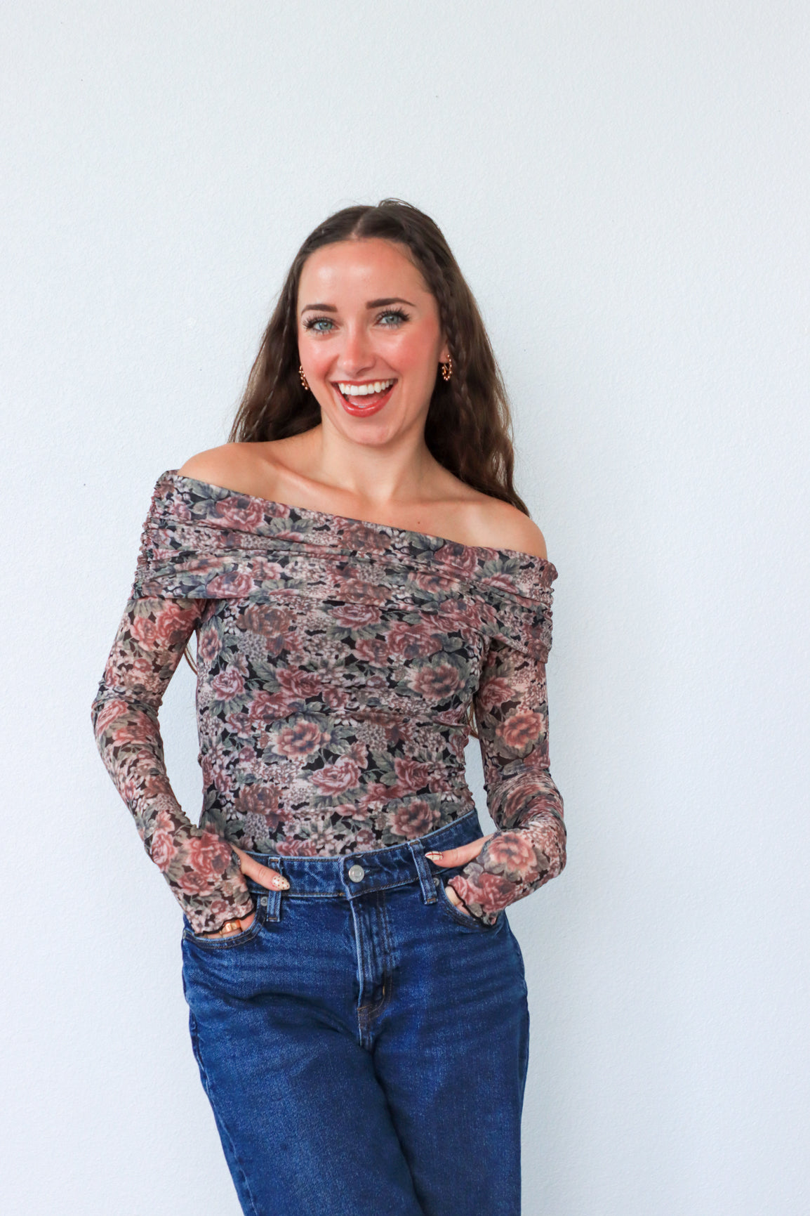 Woman wearing a floral off-shoulder top and blue jeans against a white background