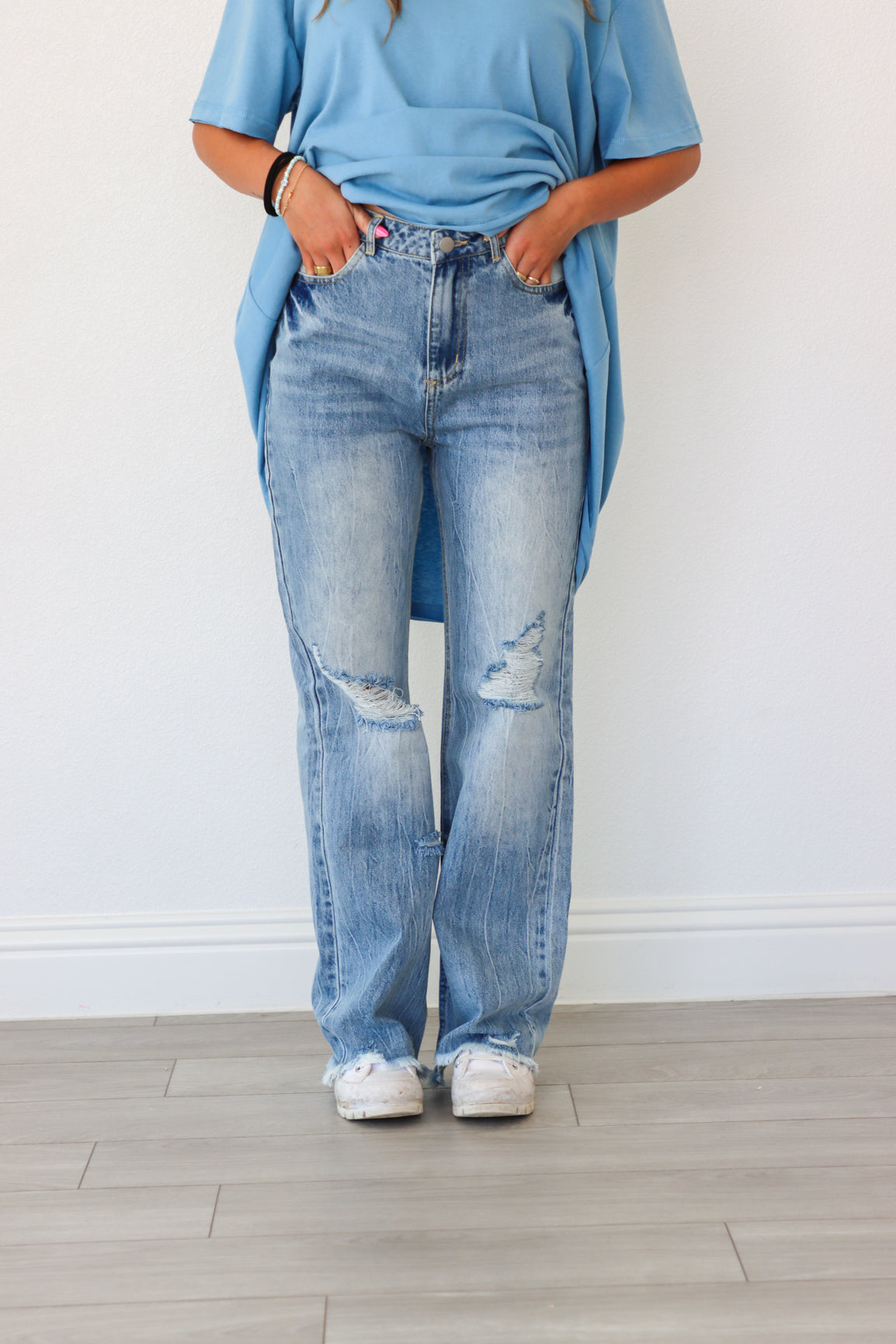 Person wearing a blue oversized shirt and light blue jeans against a white wall.