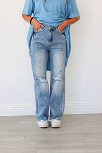 Person wearing a blue oversized shirt and light blue jeans against a white wall.