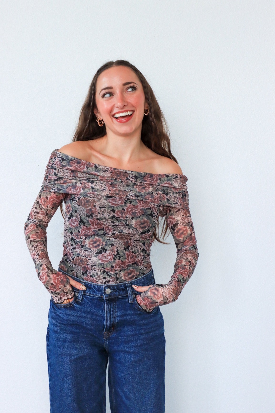 Woman wearing a floral off-shoulder top and blue jeans against a white background