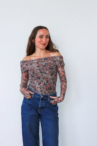 Woman wearing a floral off-shoulder top and blue jeans against a white background