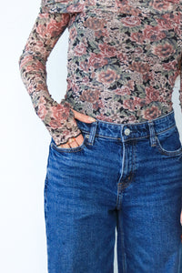 Person wearing a floral long-sleeve shirt and blue jeans on a white background