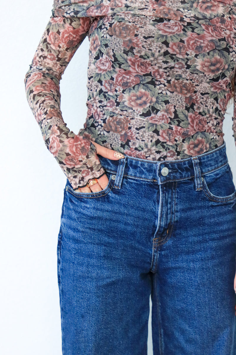 Person wearing a floral long-sleeve shirt and blue jeans on a white background