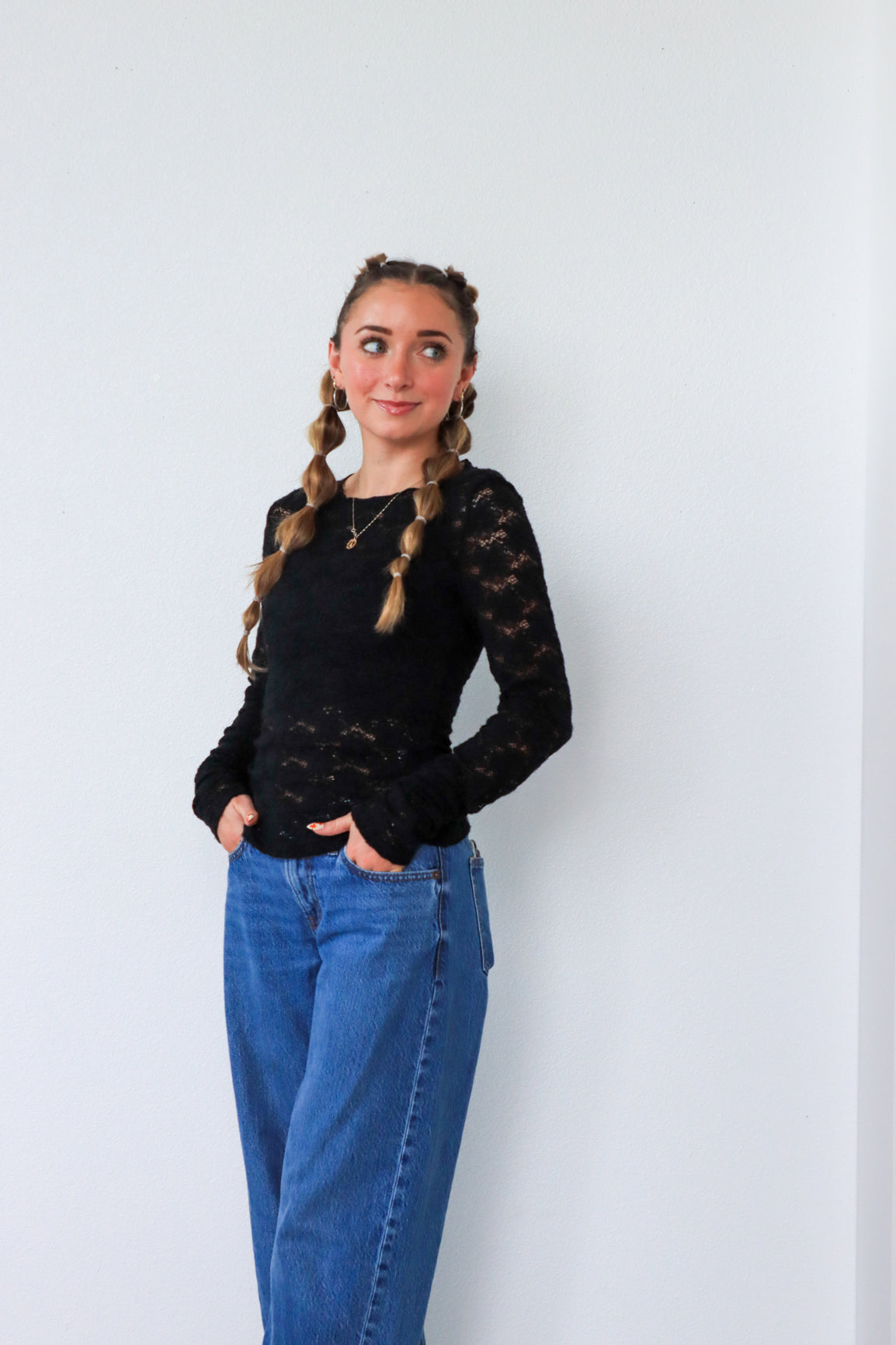 Person wearing a black lace top and blue jeans against a white background