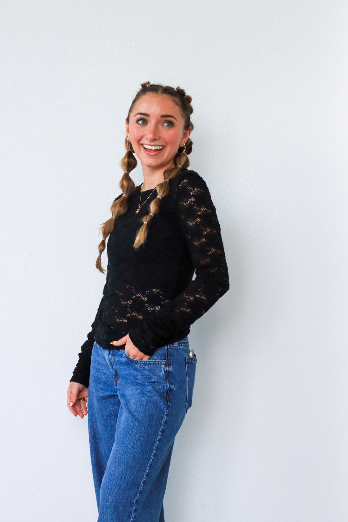 Woman wearing a black lace top and blue jeans against a white background